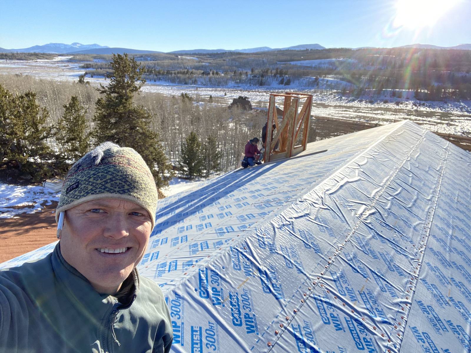 Kurt Ulrich on a wrapped roof deck under construction, with a snowy valley and mountains behind