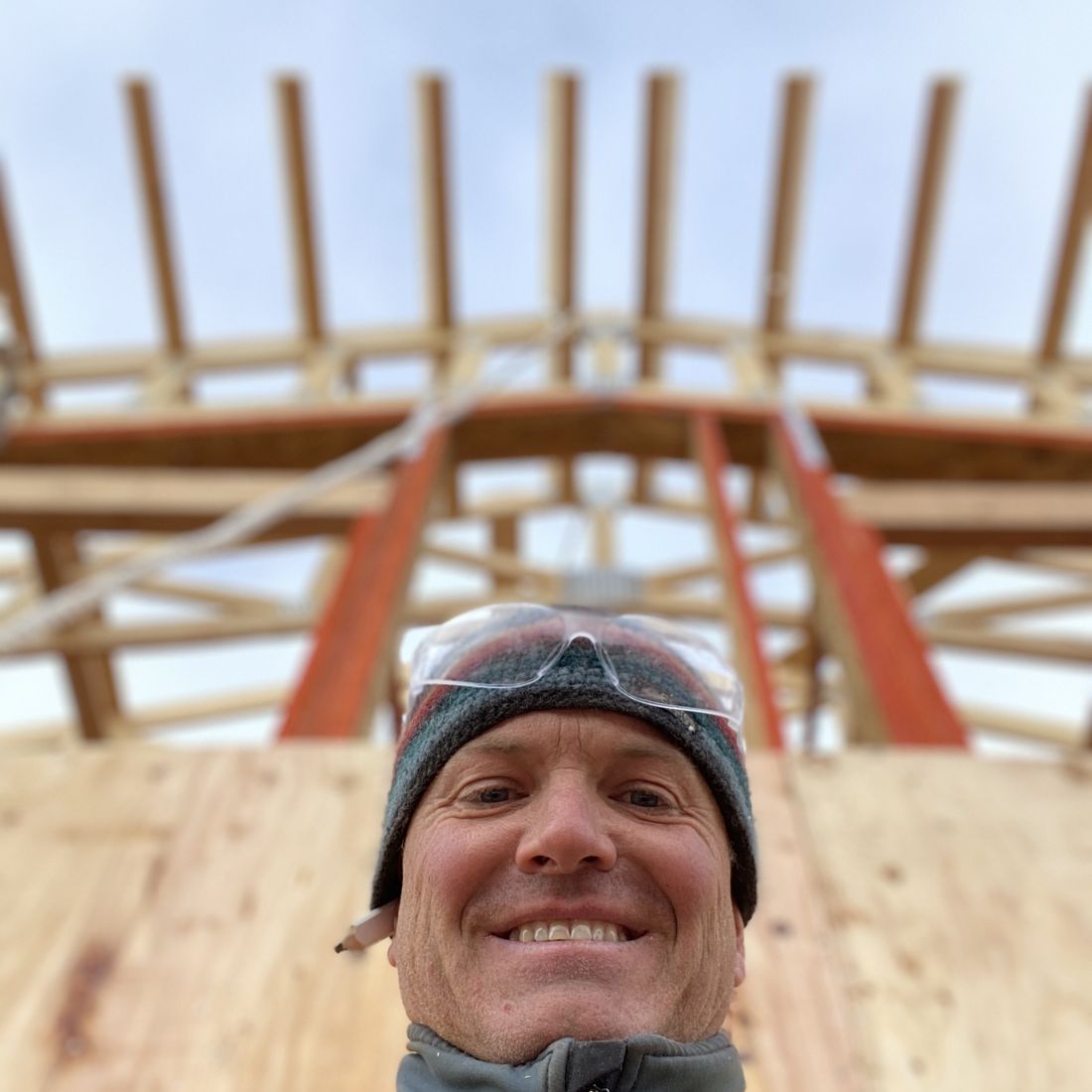 Kurt Ulrich smiling up at the camera from a roof deck, with new rafters and steel beams overhead