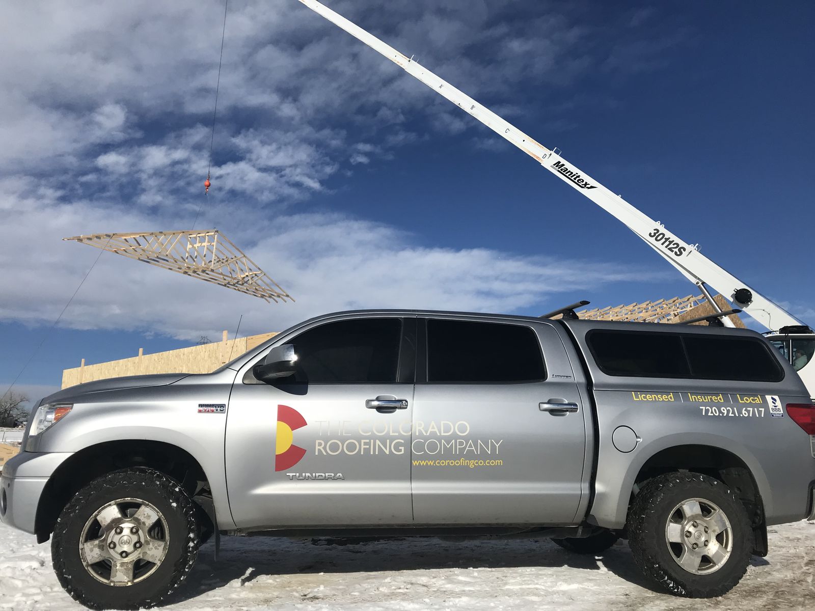The Colorado Roofing Company pickup at a build site, with a crane lifting roof trusses into place behind it